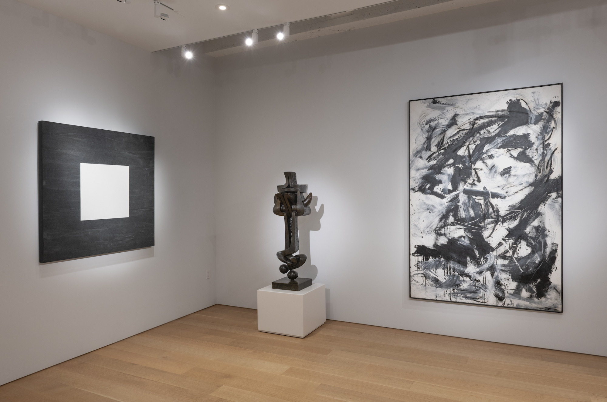 Gallery view of three pieces. One painting that is a black square with a white square in the center. Next to that is a sculpture, which is next to a black and white abstract expressionist image.